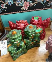 Front view of two green glazed ceramic Foo Dog figures and two red Foo Dog figures behind them on wooden floor, showing overall condition and design.