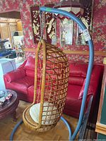 Full view of egg-shaped wicker hanging chair suspended from curved blue metal stand.