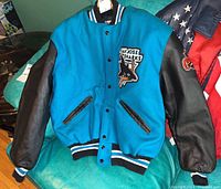 Front view of varsity style jacket showing teal fabric body, black leather sleeves, snap buttons, and San Jose Sharks logo patch on left chest.