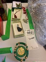 Overview of multiple jade charms and green jade bracelet with gold medallion; charms displayed in boxes and loose on table.