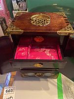 Large wooden jewellery box with double doors open showing pink floral fabric lining inside and brass lock on top