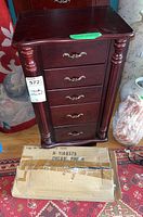 Front view of the wooden jewelry chest showing five drawers and two partially detached carved legs on either side.