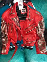 Front view of red leather biker jacket with silver studs and belt on teal background.