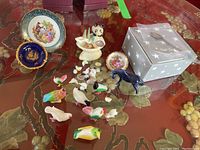 Photo showing two miniature Limoges plates, one standing in a metal holder. Several porcelain bird figurines in pastel colors, two black horse figurines, small white dove figurines, and a boxed collector spoon.
