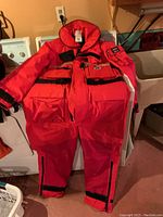 Full view of the red Mustang Ocean Class floater suit laid out on a surface showing front design and pockets