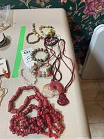 Overview of multiple necklaces and bracelets made from semi-precious stones including red coral-style beads, multi-colored chunky stone beads, and pendant necklaces with carved or donut-shaped stones.