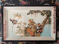 Full view of the large framed shadow box with Asian motif showing birds, flowers, tree branches, white mat and black frame with Asian script.