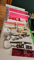 Photo showing 12 ladies watches including boxed pieces with pink interiors and various strap materials and colors