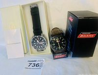 Photo showing both watches, one Dickies watch with brown leather strap and one stainless steel black face watch in box with instruction manual.