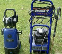 Two Simoniz spray washers outdoors on grass; left unit is electric model 1700S with hose reel, right is gas model 2000 with engine and hose coiled on frame.