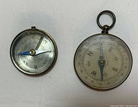 Both vintage pocket compasses shown from the top view, highlighting their size, design, and condition.