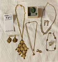 Overview of all jewelry items arranged on white background showing gold-tone and silver-tone necklaces, earrings, bracelet, ring, and a green enamel brooch in box.