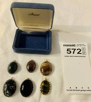 Six oval handcrafted gemstone charms and a blue velvet presentation box branded 'Anson'