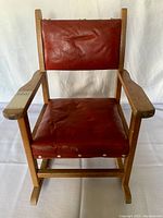 Front view of vintage child's rocking chair showing brown leather seat and back with solid maple wood armrests and frame.