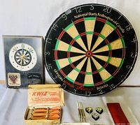 Image showing full set: Nodor dartboard, King's Stag dart clock, Kwiz darts in box, additional darts and accessories on white surface.