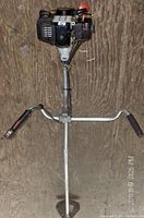 Full view of brush cutter showing engine, metal shaft, and U handlebar with grips and control switches.