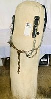 Full view of the off-white canvas punching/kicking bag standing upright with black reinforced straps and attached metal chains for hanging.