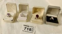 Four ladies rings each in a separate presentation box, showing different colored stones: purple, white, deep red, and clear pear-shaped crystal.