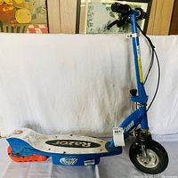 Side view of the blue Razor electric scooter showing frame, deck, and wheels with wear and dirt.
