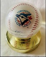 Front view of Toronto Blue Jays logo and autographs on the baseball inside a clear plastic display case with a gold-colored base.