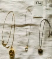 Three vintage pendant necklaces laid flat on fabric background, showing different chain styles and pendants including gold-tone Thomas Kinkade embossed locket watch pendant.