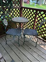 Full view of bistro set with table and two woven metal chairs on wooden deck against lattice background.