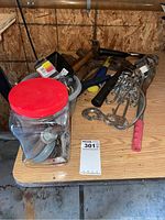 Overview of various tools and hardware arranged on a wooden surface including block and tackle, chain, and plastic container with small items.