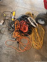 Top-down view showing mixed pile of extension cords with yellow hanging trouble light on left.