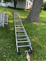 Full view of the aluminum extension ladder lying on grass with wheels attached at the base.