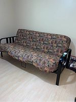 Front view of futon showing patterned upholstered mattress on black metal frame.