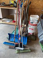 Garden tools including rakes, shovels, snow shovel, brooms, dust pans and white and red pails.