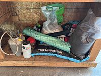 Photo showing bags of soil, including Terreau Premium bag, garden sprayers and plastic sheeting on wooden shelf.