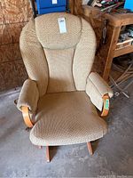 Front view of the beige upholstered glider rocker chair showing padded armrests and wooden accents.