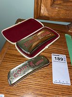 Photo showing both harmonicas, the larger Hohner Comet in its white case with red velvet lining and smaller harmonica placed beside it.