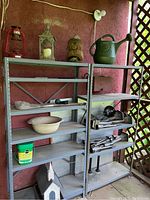 Shelf with lanterns, watering can, plant food, carved monkey, and assorted garden tools