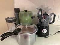 Photo showing all kitchen appliances together: green thermos, green West Bend coffee percolator, silver Presto pressure cooker, and Black+Decker food processor with attached container and accessories inside.