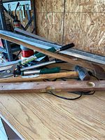 Photo showing wooden spirit level, three metal levels, garden shears, cutter, small axe, sledgehammer on wooden table against plywood wall
