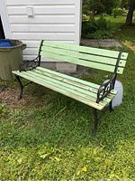 Full side view of park bench showing green painted wooden slats and decorative cast iron frame on grass.