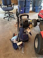Full view of Simoniz pressure washer unit on wheels with hose reel and various cleaning attachments scattered at the base and hanging on the unit.