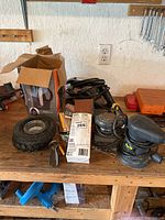 Photo showing assortment of tools including palm sanders, planer, sanding belts, tire ashtray, and storage box with casters on wooden workbench under wall outlet.