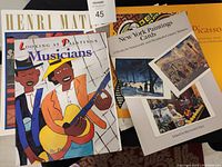 Photo of assorted art-related books and calendars including Looking at Paintings Musicians book, New York Paintings Cards postcard book, and partially visible 1999 Picasso calendar.