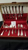 Full set of flatware pieces arranged in lined case with red velvet-like interior, showing knives in top lid and forks, spoons, spreaders in bottom section.