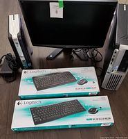 Two desktop computers (Dell and HP) flanking an Acer widescreen monitor on a table with two Logitech wireless keyboard and mouse combo boxes in front of the monitor.