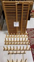 Four wooden plate racks in varying sizes arranged on the floor, showing the large slatted rack standing and the smaller peg racks in front.