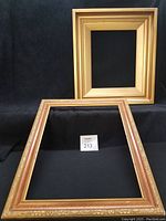Two gold frames placed against black background, showing front of classic smooth frame and ornate detailed frame.