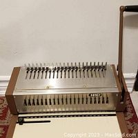 Full view of the HIC HPB 210 manual binding and punching machine showing metal construction, lever handle, and punch slots.