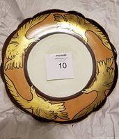 Photo showing full front of the circular cabinet plate with hand painted eagles flying on the rim, in gold color against a tan and brown border and a white center.