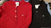 Red long sleeve Henley shirt and black sleeveless polo shirt showing Lacoste logos and button details.