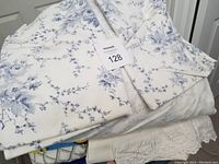 Close up of floral print bed cover and sheets, folded and stacked with some pillowcases beneath