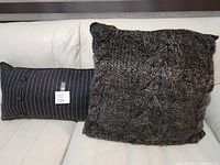 Two grey cushions on white surface, includes one knitted square cushion and one pinstripe rectangular cushion with buttons.